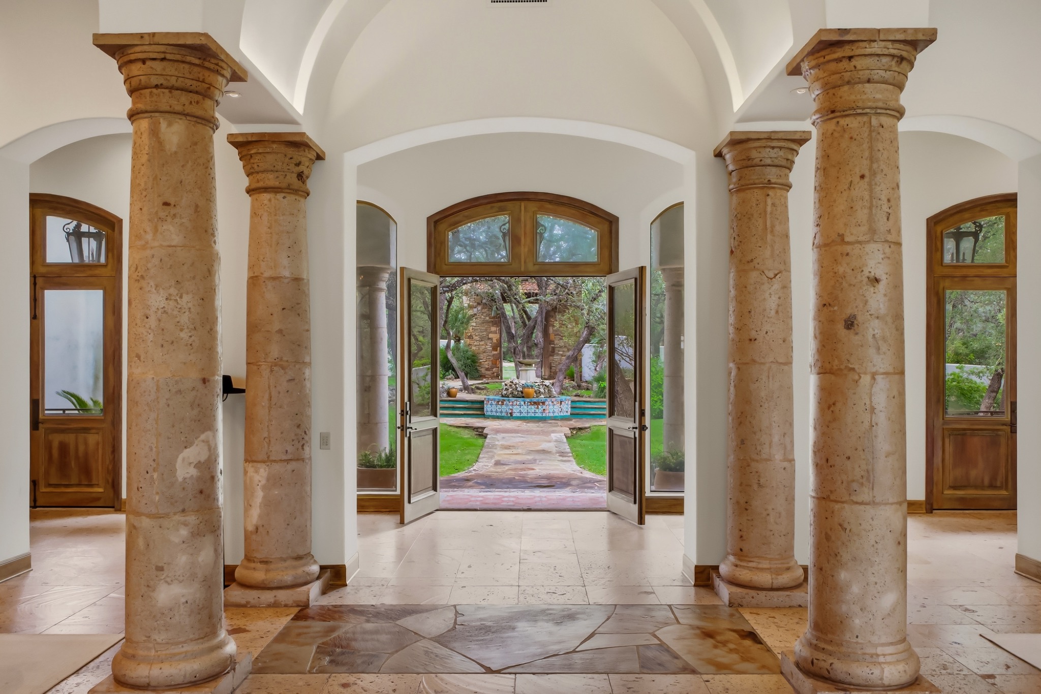 Grand home entrance with open doors and a landscaped courtyard beyond